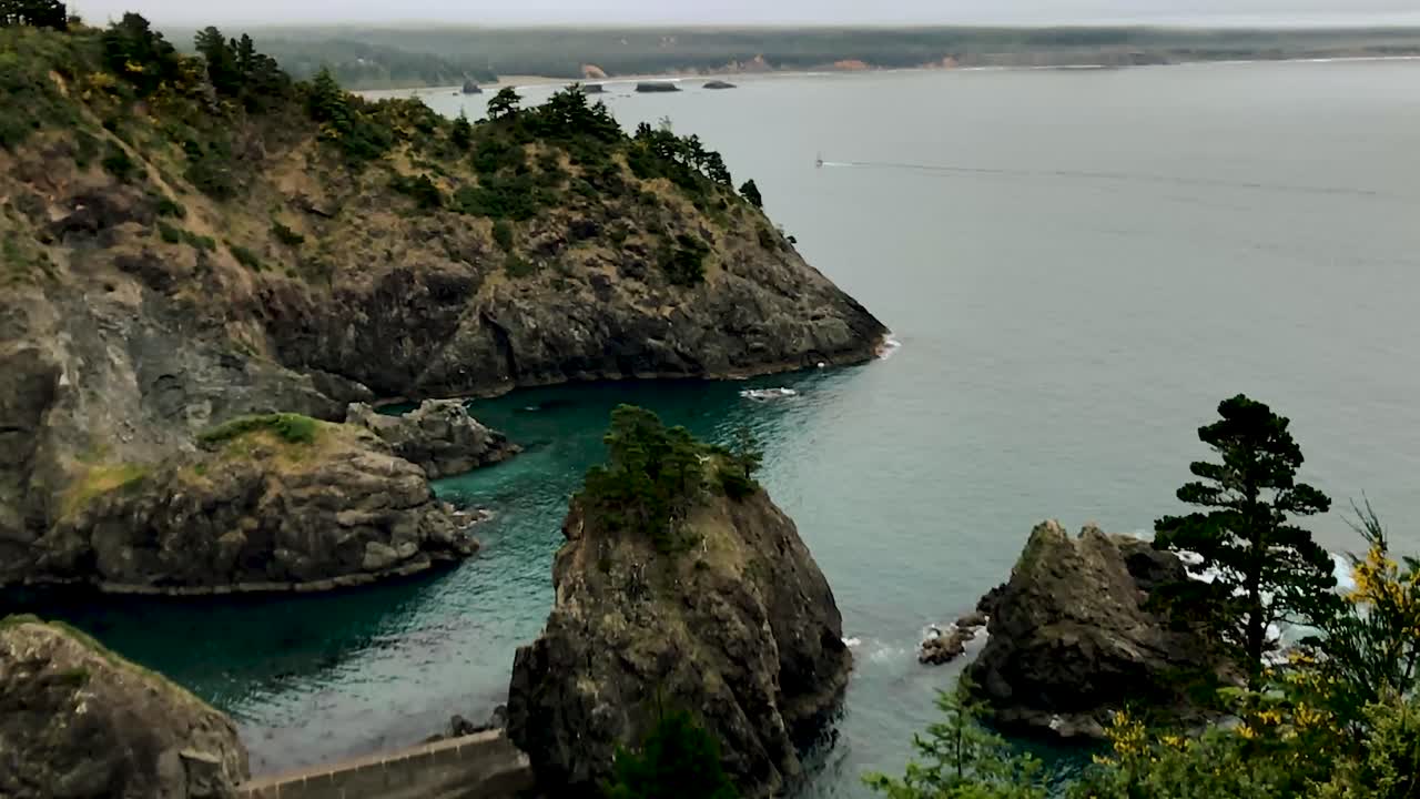 una vista del océano pacífico de un barco que pasa por acantilados en la distancia por port orford heads, oregon en el noroeste del pacífico