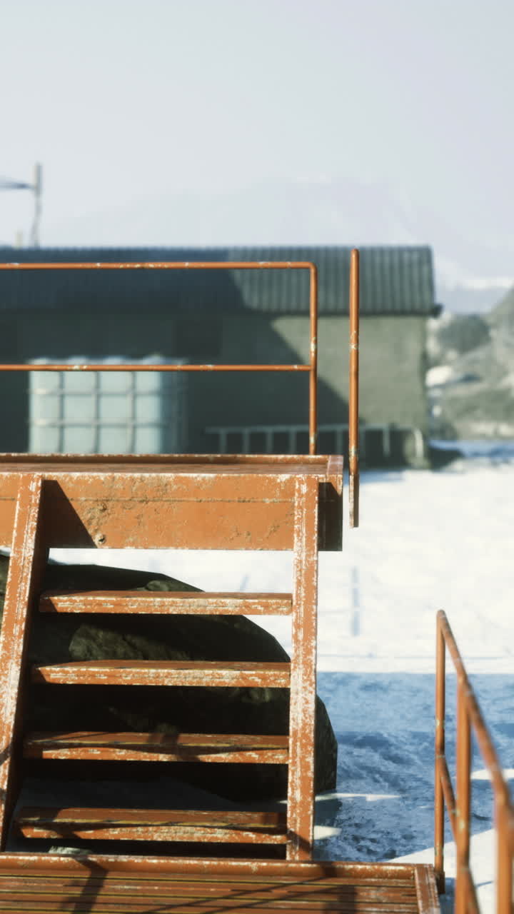 Metallplattform und Treppe nahe einer Lagerhalle in einer verschneiten Landschaft.