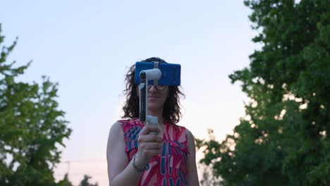 mujer joven con gafas probando innovador nuevo insta360 flujo estabilizador de gimbal de cámara móvil al atardecer