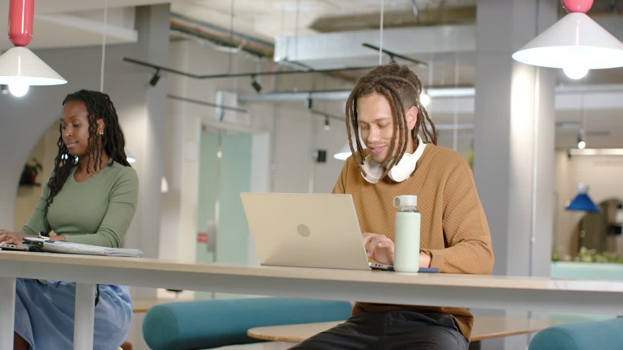 Colegas de trabalho afro-americanos começando o trabalho, digitando em laptops, verificando anotações em uma mesa compartilhada.