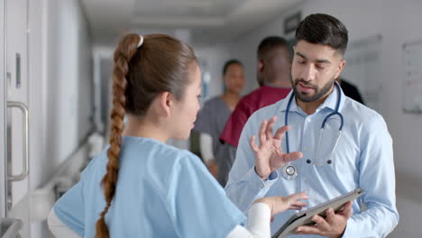 diversos médicos masculinos y femeninos discutiendo el trabajo usando tableta en el pasillo del hospital, en cámara lenta