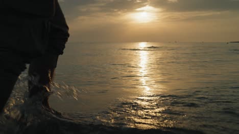 close up feet of male walking on the beach in the water at sunrise slow motion