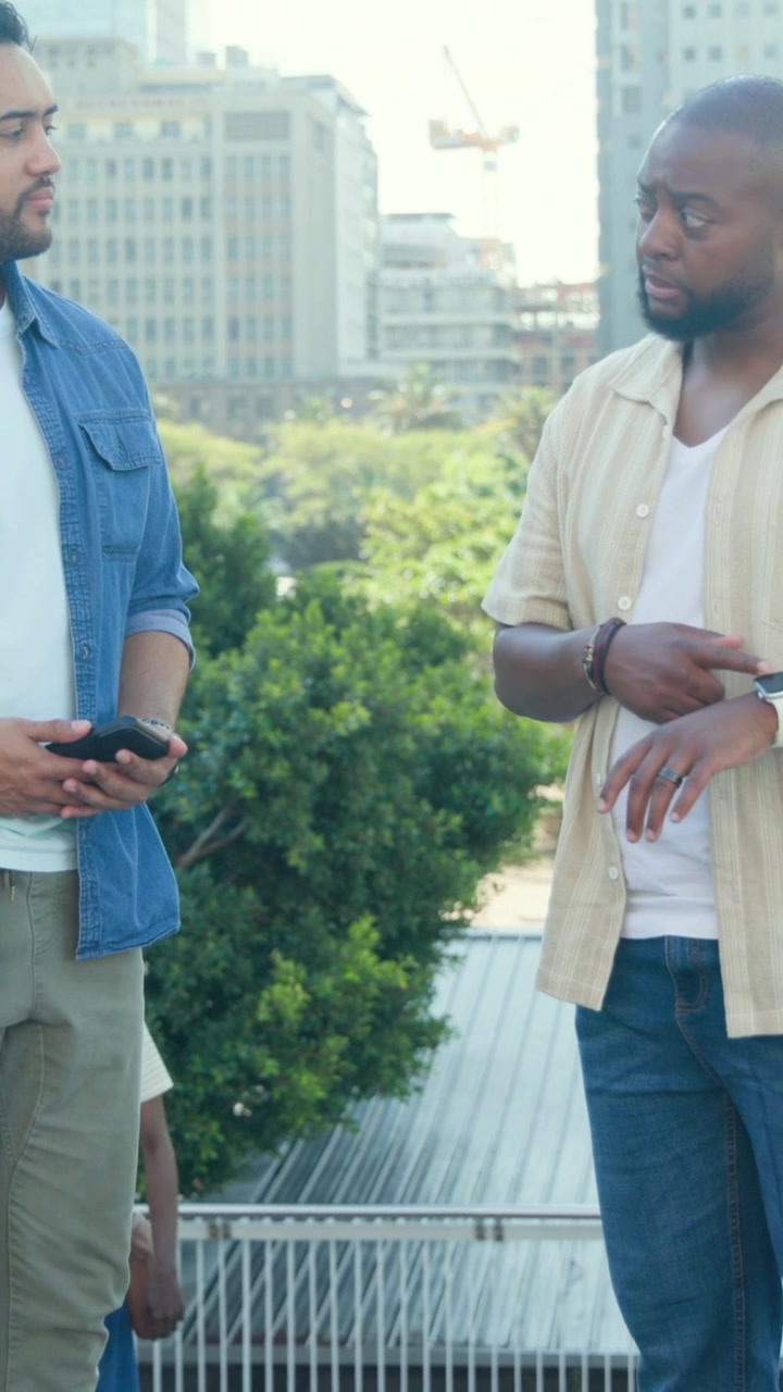 Denim man holding phone while peer approaching and checking watch, planning business meet near rail