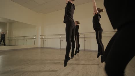 a group of young ballet students in black dancewear practicing positions in a spacious ballet studio with wooden flooring and wall-mounted barres. focused expressions and synchronized movements.