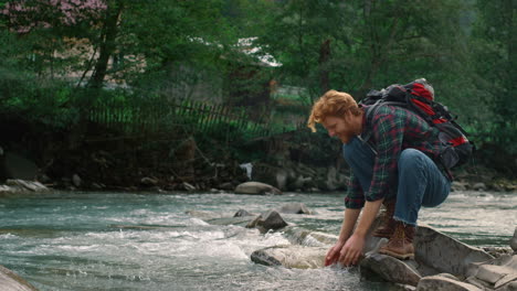 Mann-Sitzt-Auf-Einem-Felsen-Am-Fluss.-Glücklicher-Wanderer,-Der-Wasser-Aus-Dem-Gebirgsbach-Spritzt