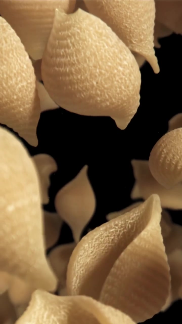 Rallentatore di conchiglie di pasta cruda che cadono su sfondo nero.