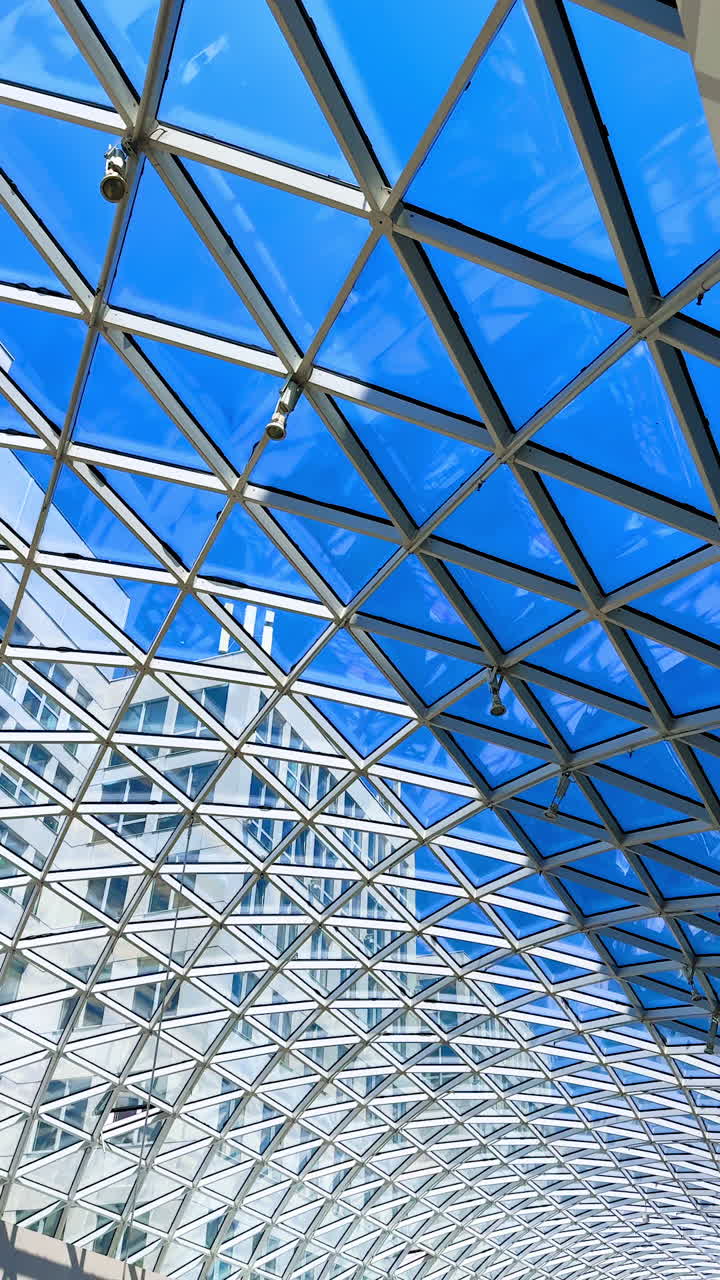 Long glass roof with metal constructions. Low angle view. Blue sky at backdrop. Vertical video.