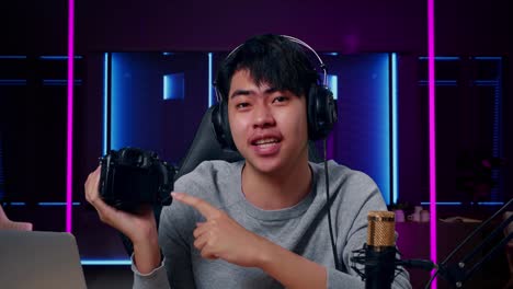 close up of a smiling asian man with computer reviewing camera in room lit by neon lights in retro