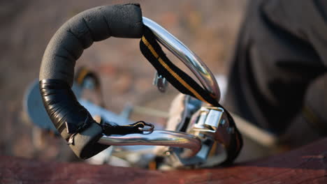 close up of metal stilt with black and orange strap, wrapped handle with black tape, and reflective metallic surface, positioned outdoors on blurred background, highlighting details of equipment