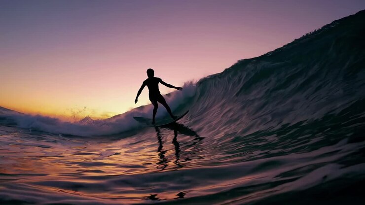 Silhouette of a surfer riding a wave at sunset, captured from a low-angle