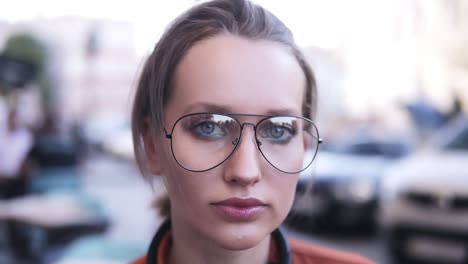 Headshot-of-attractive-blonde-woman-with-pretty-face-looking-at-camera,-standing-in-urban-surroundings-on-summer-day,-wearing