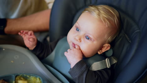 blond caucasian baby boy chewing his food. mom's hand gives vegetables to her lovely child. top view.
