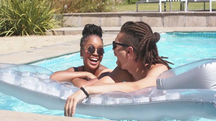 African American couple leaning on float at pool, shirtless man pointing, woman laughing, flirting