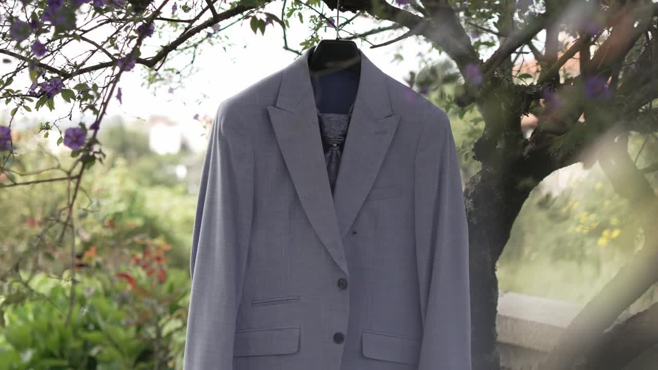 Light gray suit jacket hanging on a tree branch in a natural garden setting