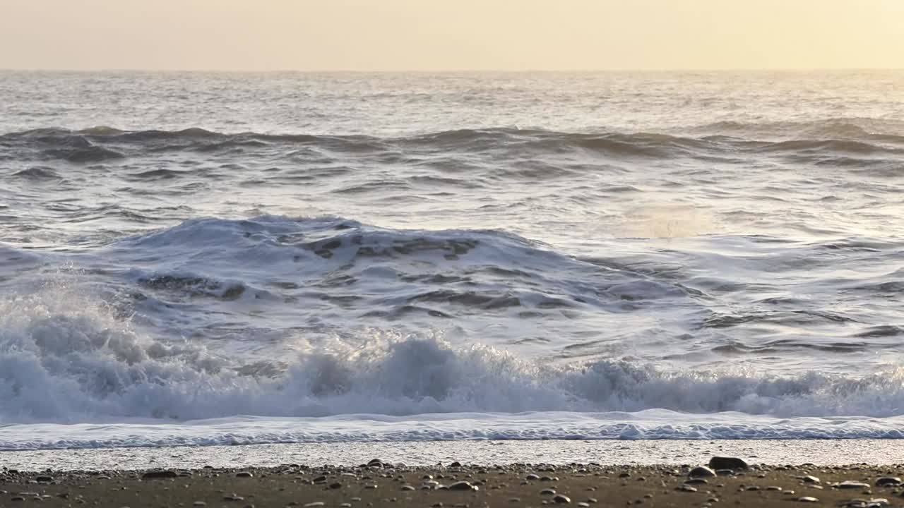 A Rough winter sea with waves crashing on a black beech in Iceland. The setting sun in the background