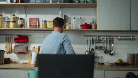hombre bailando en la cocina preparando el desayuno. hombre contestando una llamada de video en la computadora portátil.