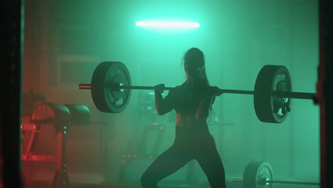 slow motion: athletic beautiful woman does overhead deadlift with a barbell in the gym. female professional bodybuilder workout weight lift exercises in the authentic sport training facility.