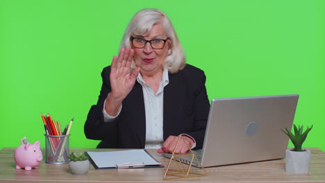 Senior-business-woman-waves-hand-palm-in-hi-gesture-greeting-welcomes-someone-webinar-at-office