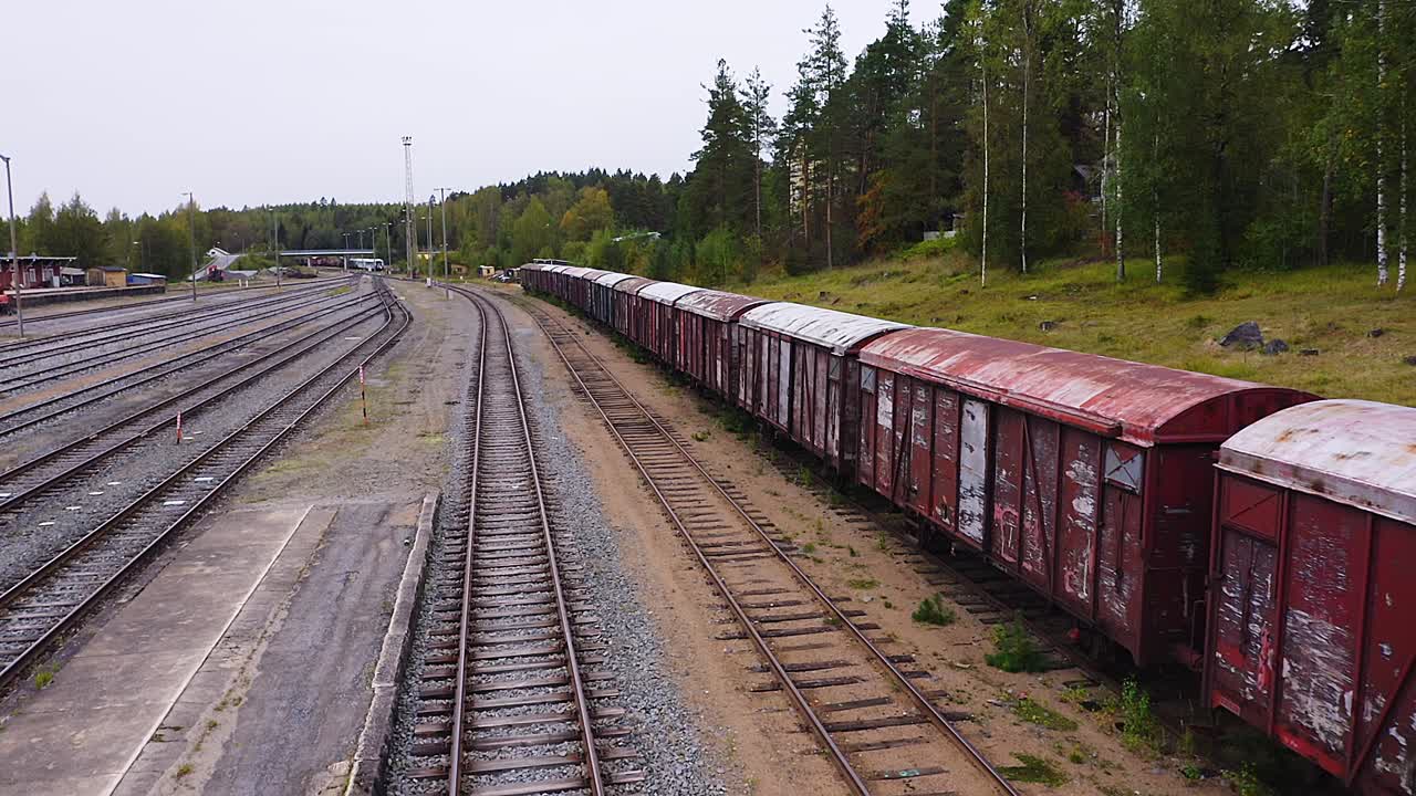 Tracking drone view of multiple old and rusty railroad wagons abandoned on the side track of a railyard in Finland.