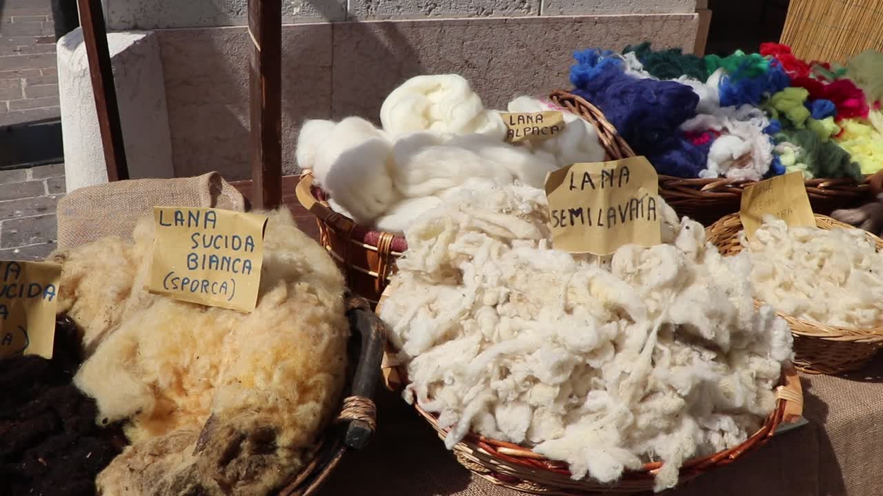 Cesti pieni di lana di pecora e alpaca grezza e semilavata esposti in un mercato storico medievale in Italia.