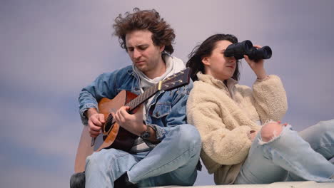 a young boy plays the guitar and a young girl looks around with a pair of binoculars on the roof of a caravan 1