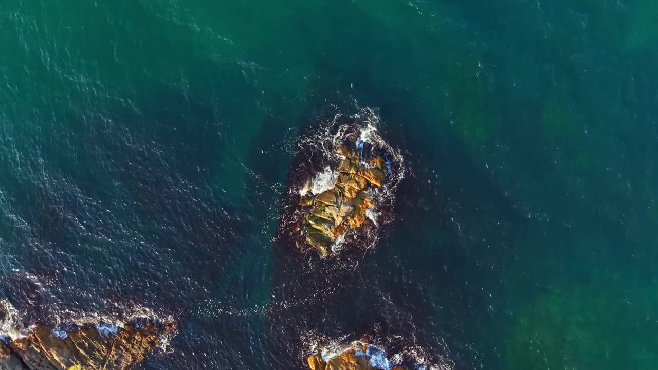 Waves crash against rocks in the ocean near a coastline during daylight hours