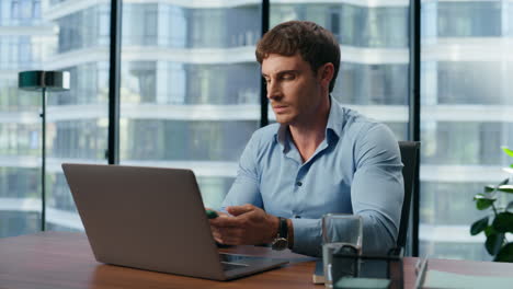 Serious-boss-answering-call-office-interior-closeup.-Businessman-typing-laptop