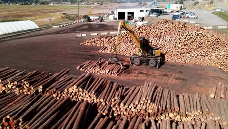 pan right zoom drone shot of a log loader at a sawmill moving logs on wood piles in a desert environment