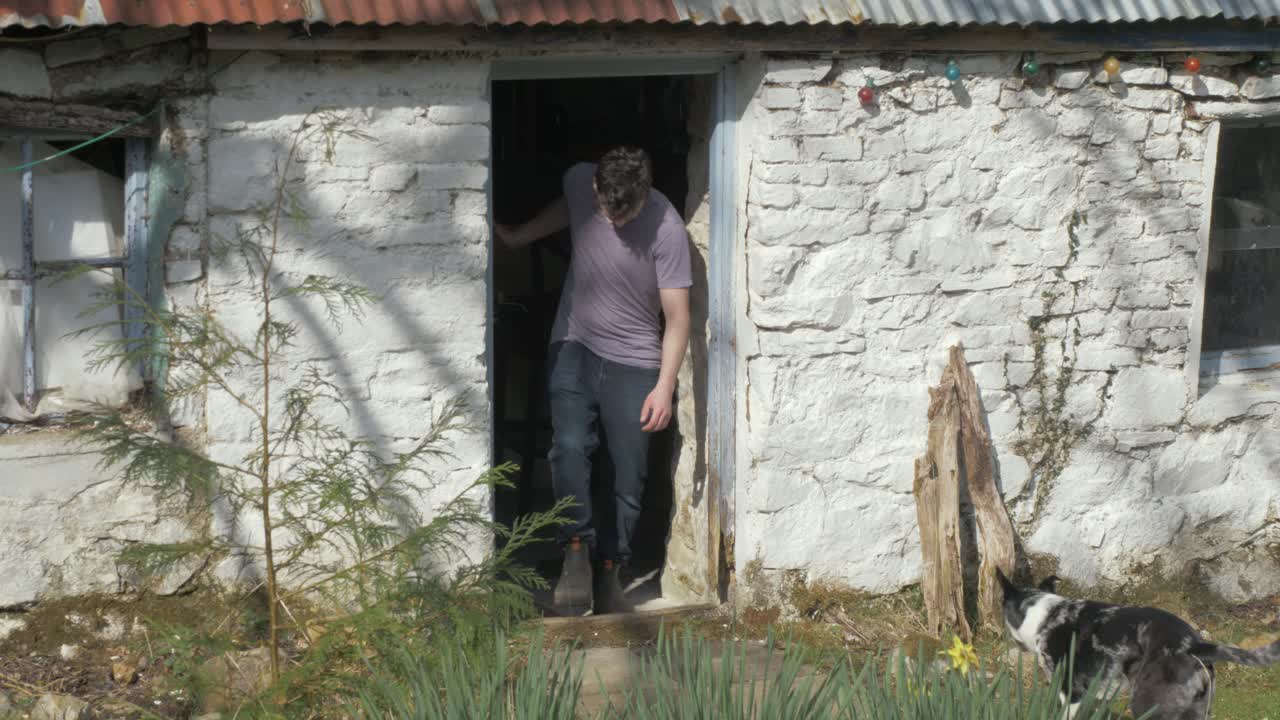 Young man exiting Irish stone cottage sunny day