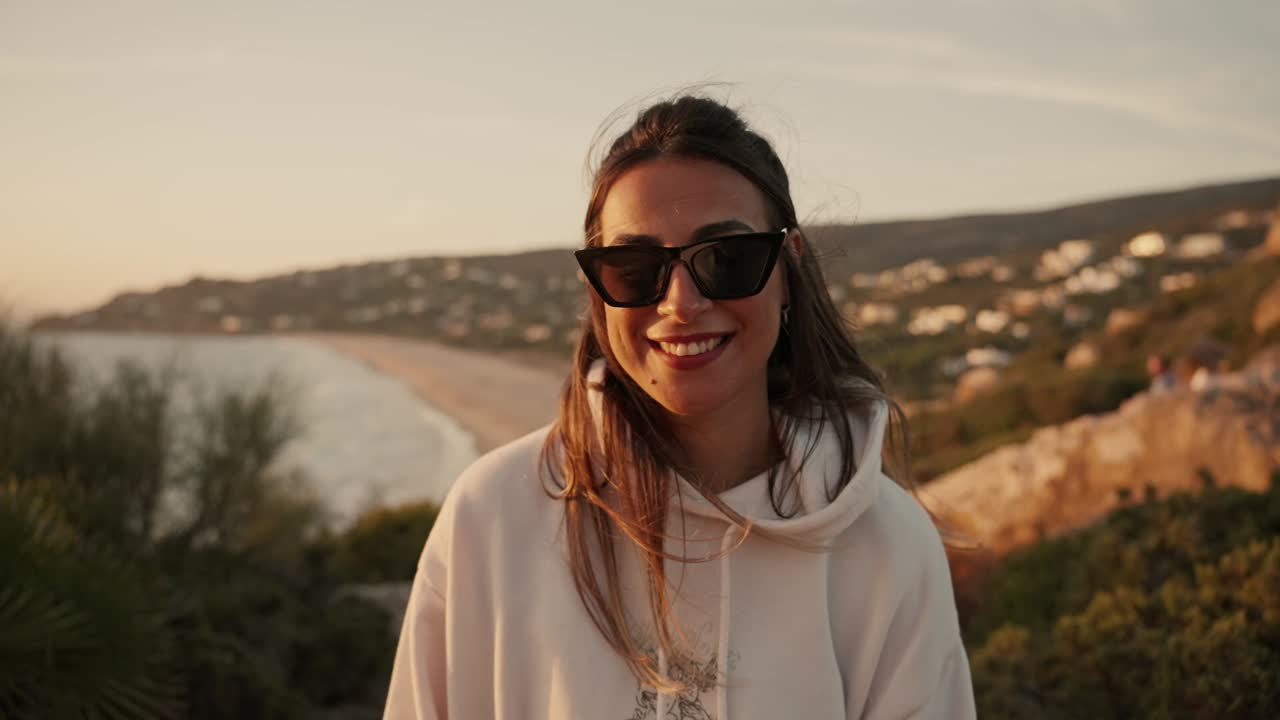vista frontal de una joven mujer española sonriendo al atardecer con vistas al mar