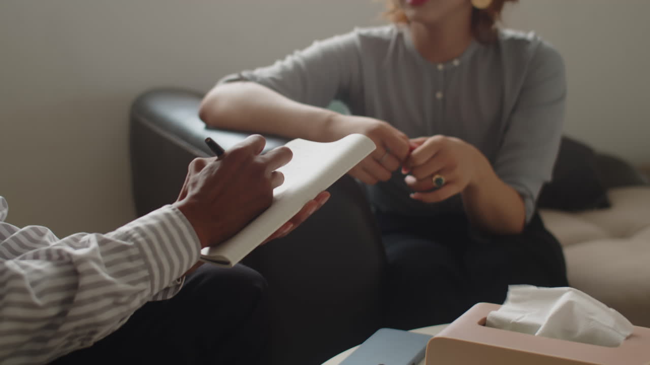 Unrecognizable Therapist Writing in Textbook Listening to Patient at Session
