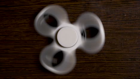 white fidget spinner spinning on a dark wooden surface