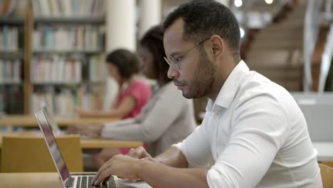 vista lateral de un joven enfocado que usa una laptop en la biblioteca