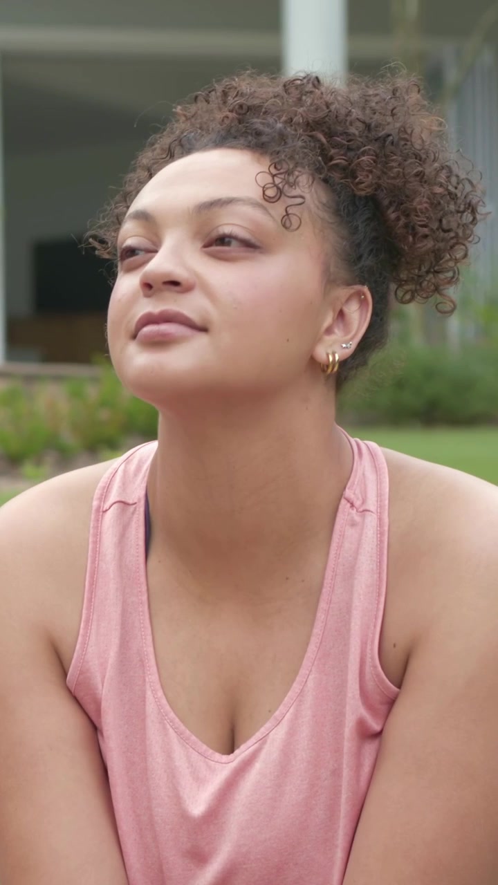 Vertical video: Camera moving, woman tilting resting chin lifting face reflecting on yard, pink top