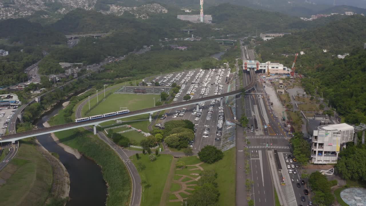 4k Arial 4K Drone paning right, View of Metro Train Passing Through Green Urban Landscape with River and Parking Lot — Modern Smart City Transportation Concept