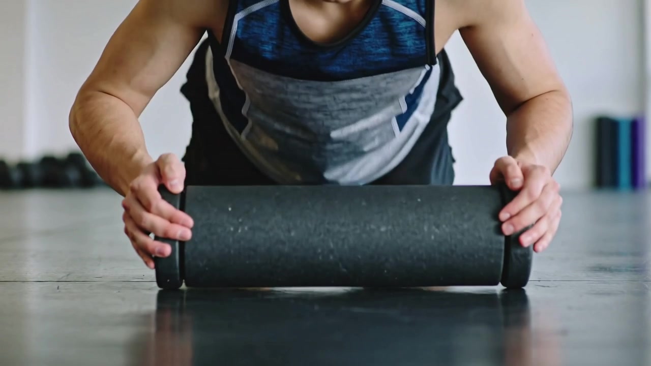 Gripping black roller, fit man wearing navy top and black shorts rolling at gym warming up