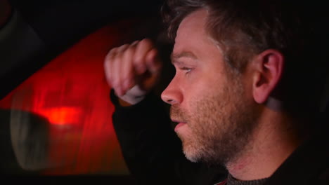 a sad man alone in a car at night with traffic passing on a busy road