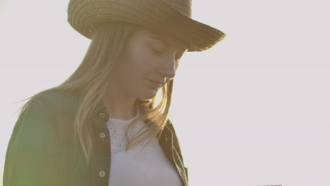 A-female-farmer-in-a-plaid-shirt-with-a-tablet-computer-in-her-hands-is-walking-across-a-wheat-field-at-sunset-checking.-The-quality-and-maturity-of-the-crop