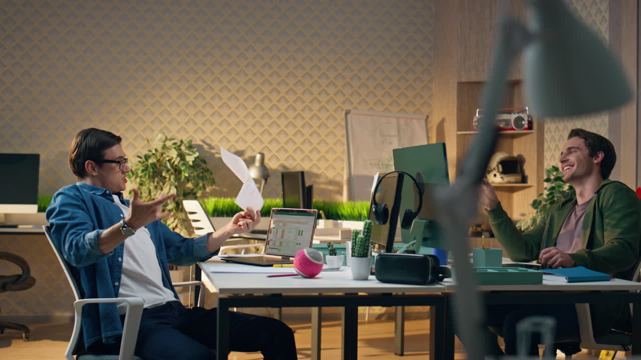 편안한 디자이너들이 크리에이티브 오피스에서 함께 소통하고, 사람들이 종이를 던지고 있다.