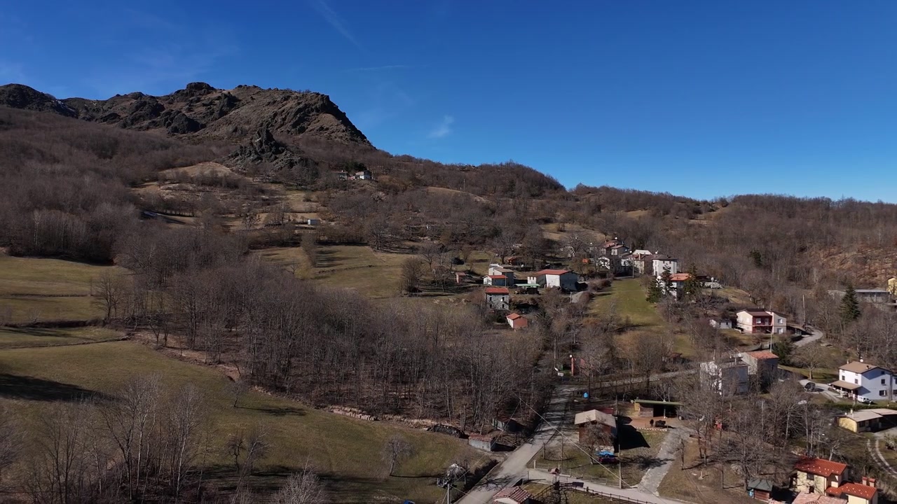 Piccolo borgo rurale vicino a Monte Lama nell'Appennino settentrionale dell'Emilia Romagna, Italia, circondato da boschi di montagna, campi terrazzati e case isolate in collina. Ripresa aerea del paesaggio con drone.