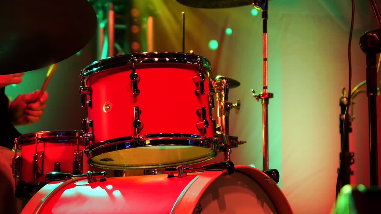 primer plano de los palos del baterista tocando en el escenario con un conjunto de tambores rojos