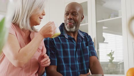 Happy-senior-diverse-couple-sitting-in-living-room-and-drinking-coffee