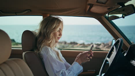 mujer usando un teléfono inteligente en un coche retro junto al mar