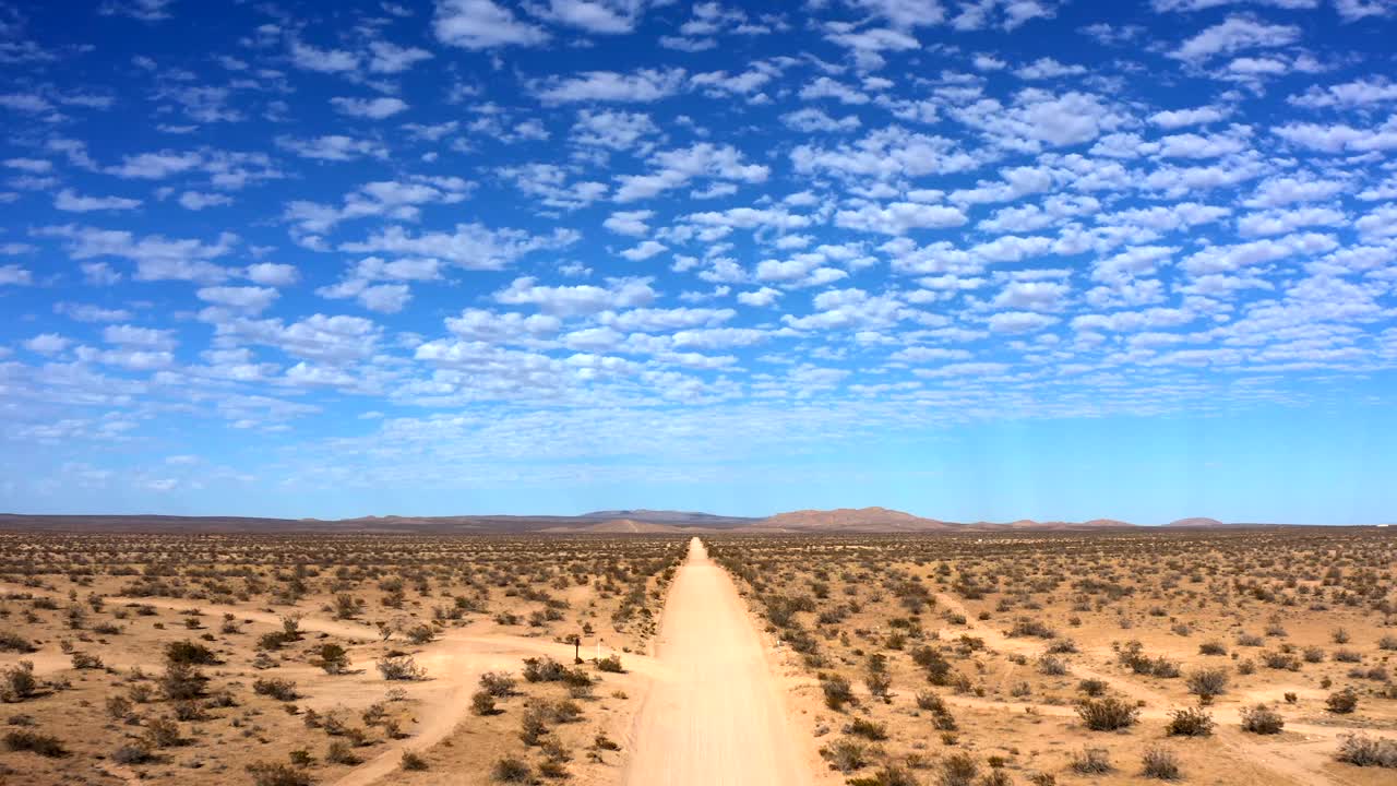 volando hacia atrás sobre el camino de tierra del desierto con cielo azul y nubes esponjosas
