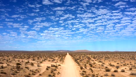 flying backward over desert dirt road with blue sky and fluffy clouds