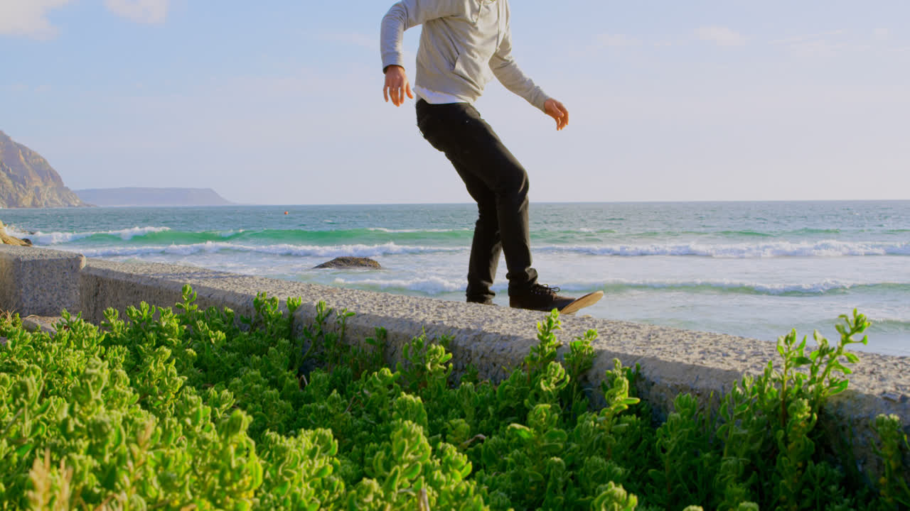 해변 4k의 보행로에서 스케이트보드 트릭을 연습하는 젊은 백인 남자의 측면 뷰