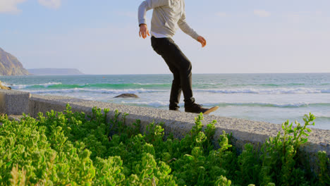 side view of young caucasian man practicing skateboard trick on the pavement at beach 4k