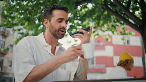 man recording voice message at cellphone sipping coffee at street closeup