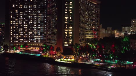 Waikiki-Hotel-Drone-Luftaufnahmen-Bei-Nacht-Mit-Hellen-Gebäuden-Und-Viel-Licht-Mit-Verkehr-Und-Palmen-Oahu-Hawaii-Mit-Farbigen-Lichtern