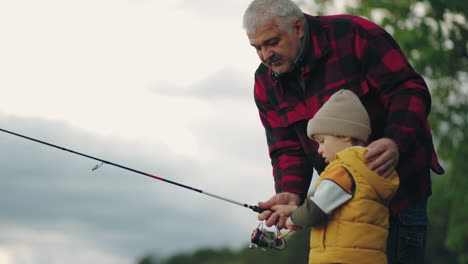 il nonno attento sta insegnando al nipote a pescare nel lago la famiglia si sta riposando in natura